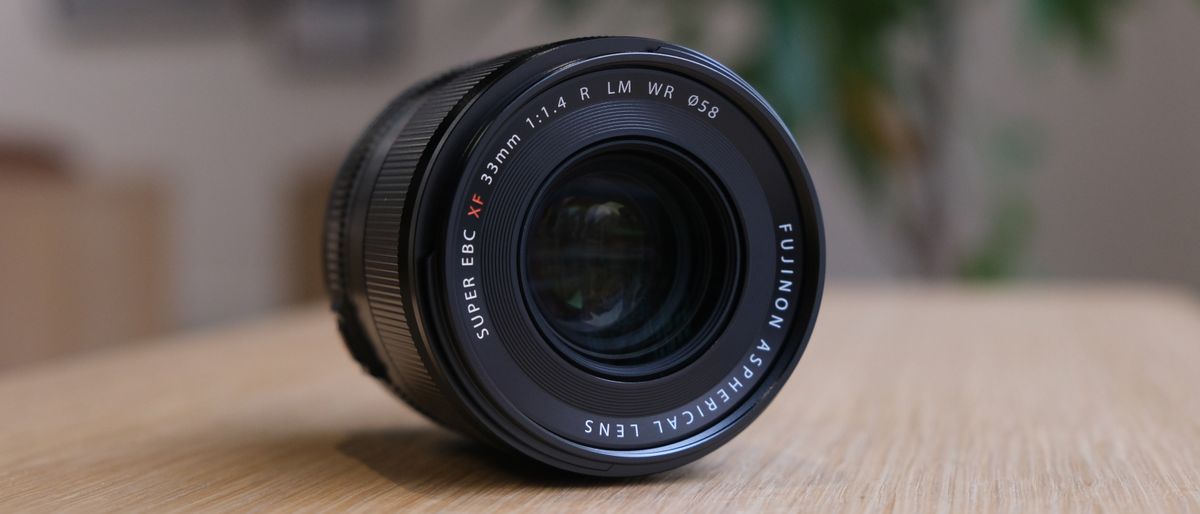 The Fujifilm XF33mm f/1.4 lens on a wooden table