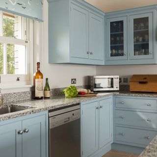 Light blue kitchen with under counter dishwasher and empty big wine bottle on top of counter