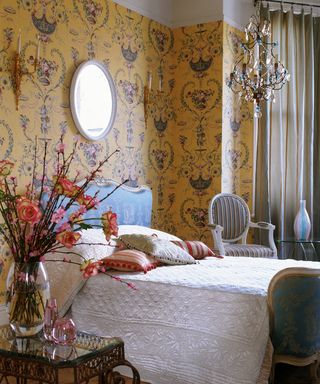 A bedroom with a chandelier and yellow rococo-style wallpaper