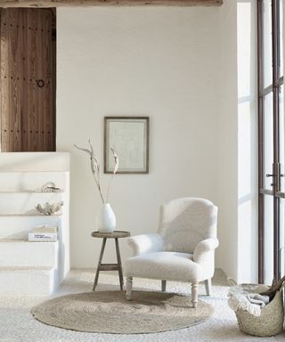 White living room with beams, armchair, side table, stairs to the left
