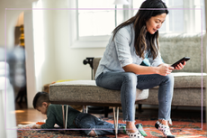 Mum looking on her phone as son plays on the floor