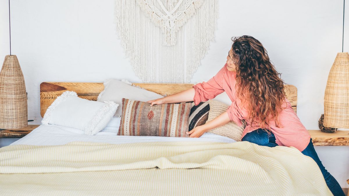 Woman arranging pillows on the bed in a brightly lit room