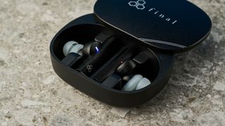 a photograph of black earbuds by final with a long, angular stem and black casing, silicone ear tips, and a black oval case reading 'final' with three decorative hexagons