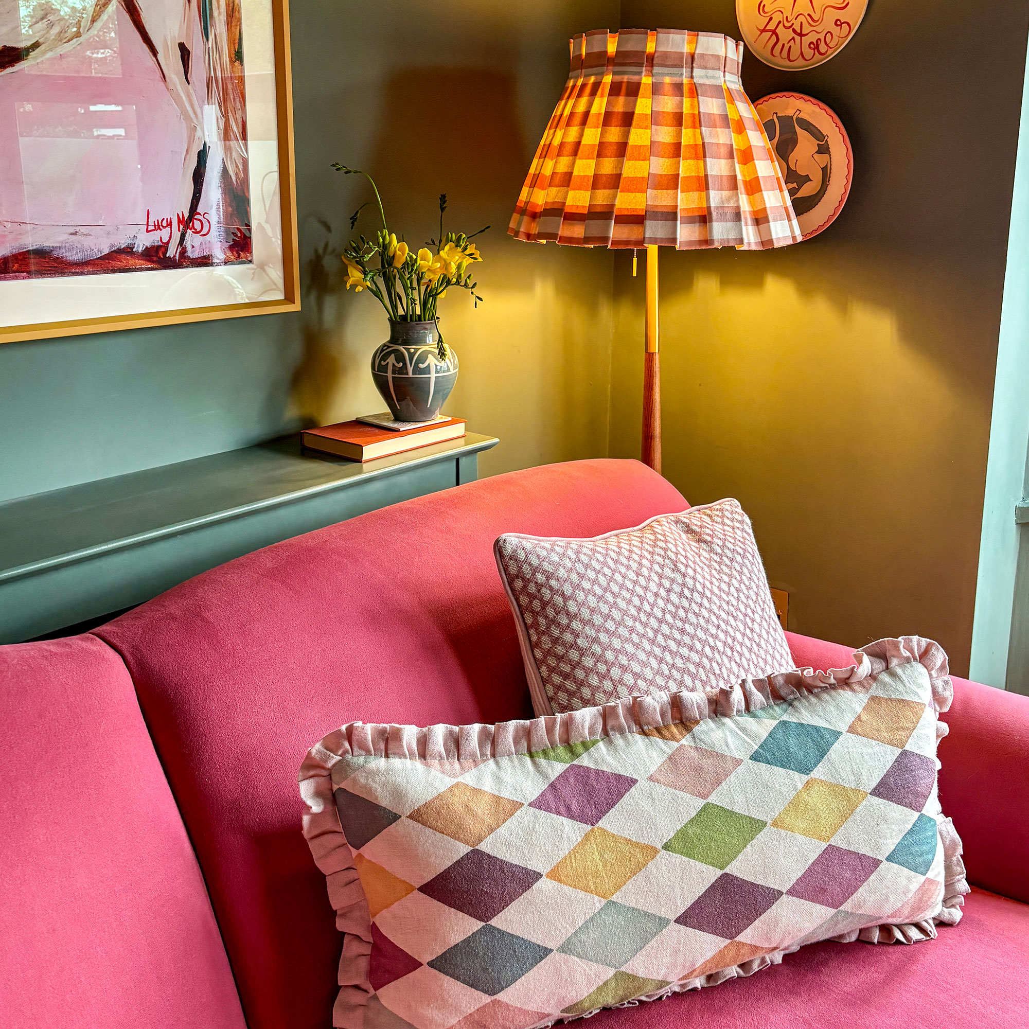 Corner of green room with pink sofa, colourful cushions and light with gingham lampshade