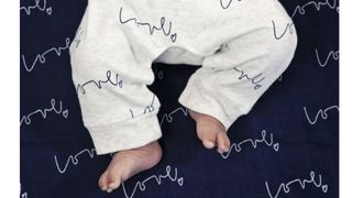 A baby's bare feet lying on a muslin swaddle printed with the word 'love'