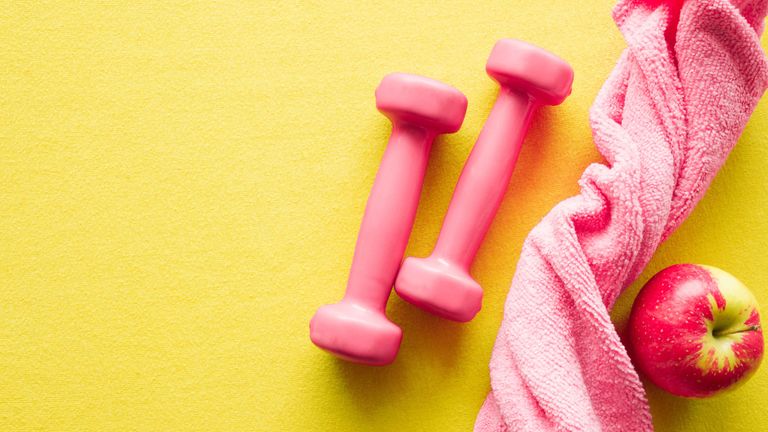 Home gym fitness equipment: yellow background with pink weights, pink towel and red apple
