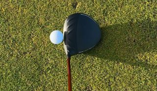 The Ping G430 Max 10K Driver at address behind a golf ball and on a green background