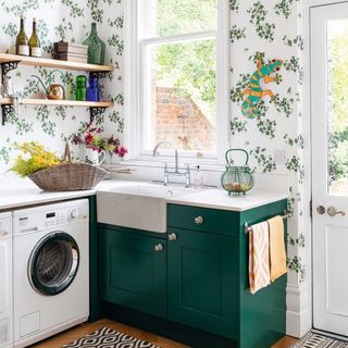 Washing machine fitted in kitchen with green painted cabinets, shelving, and patterned wallpaper