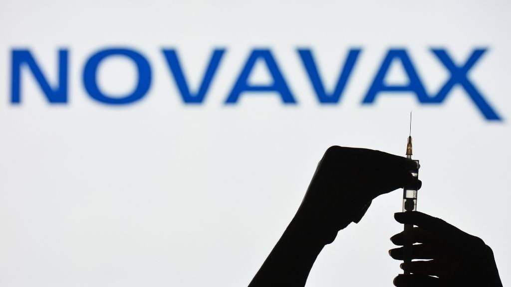 silouette of hands prepping a syringe for injection in front of white background with word &quot;Novavax&quot; written across it in blue