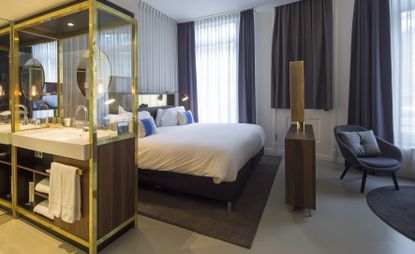 Bedroom in neutral tones with an open bathroom featuring a white marble sink and brass highlights