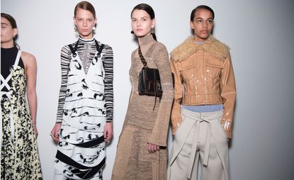 Two models in black and white dresses, one in a nude-coloured dress and one in a sand-coloured shiny jacket with off-white trousers