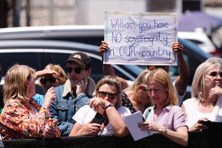 A crowd of people with one holding up a sign that says "William you have NO sovereignty in OUR country."