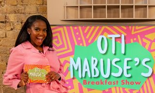 Oti Mabuse poses with her cue cards in the studio, in front of the logo for Oti Mabuse's Breakfast Show