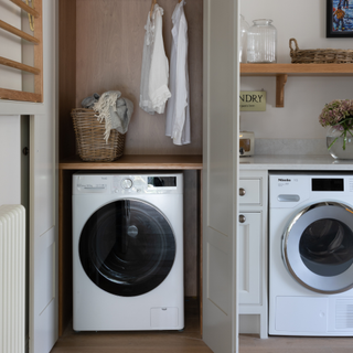 washer an drier serperated by a wall. Above the washing machine are two hanging shirts and a box of laundry