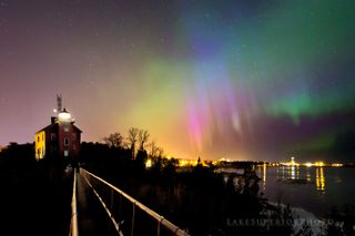 Rainbow-colored northern lights glisten above a lighthouse on the shore of Lake Superior.