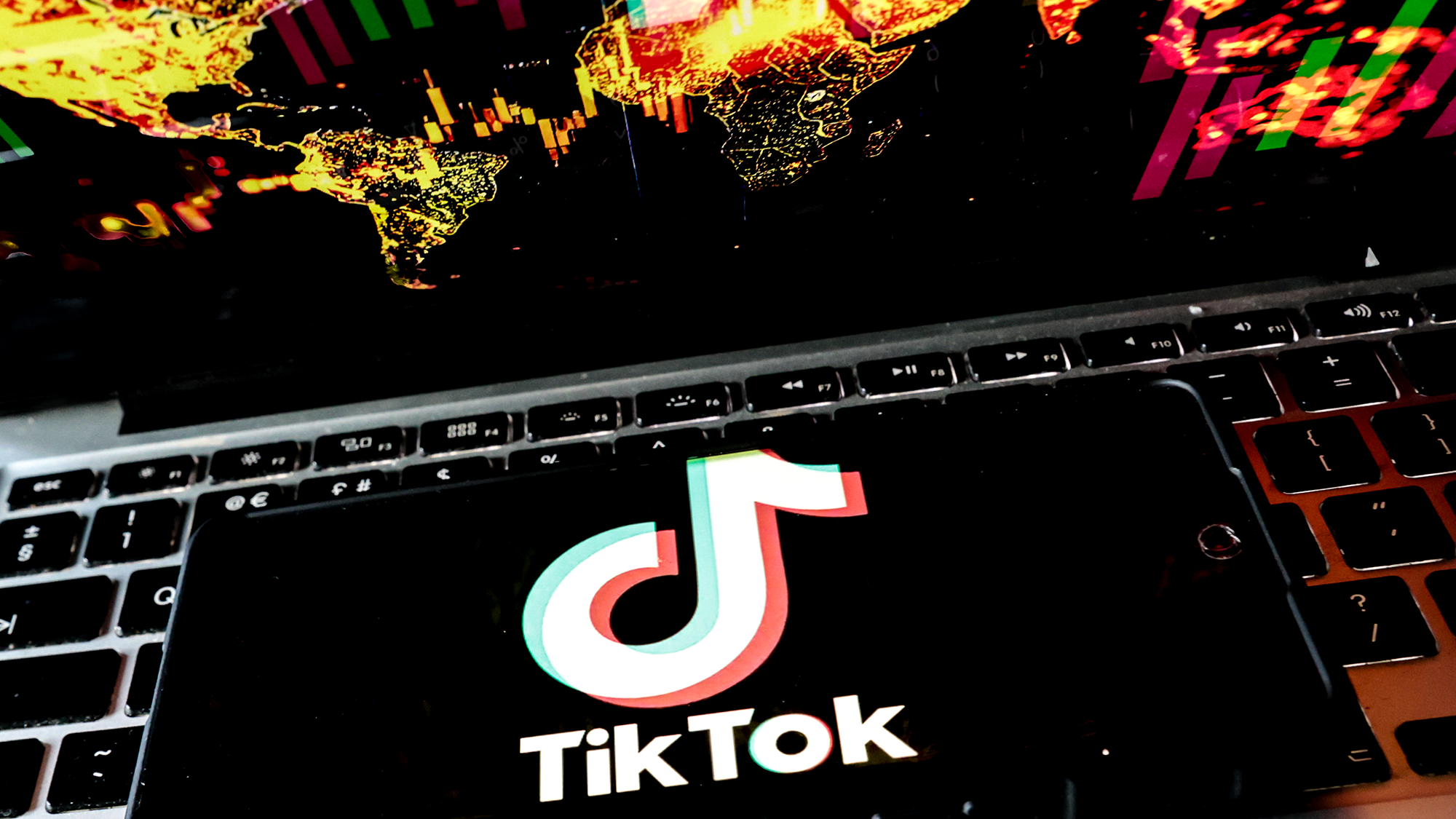 A close up of a phone laying on a laptop keyboard with the white "TikTok" logo on it