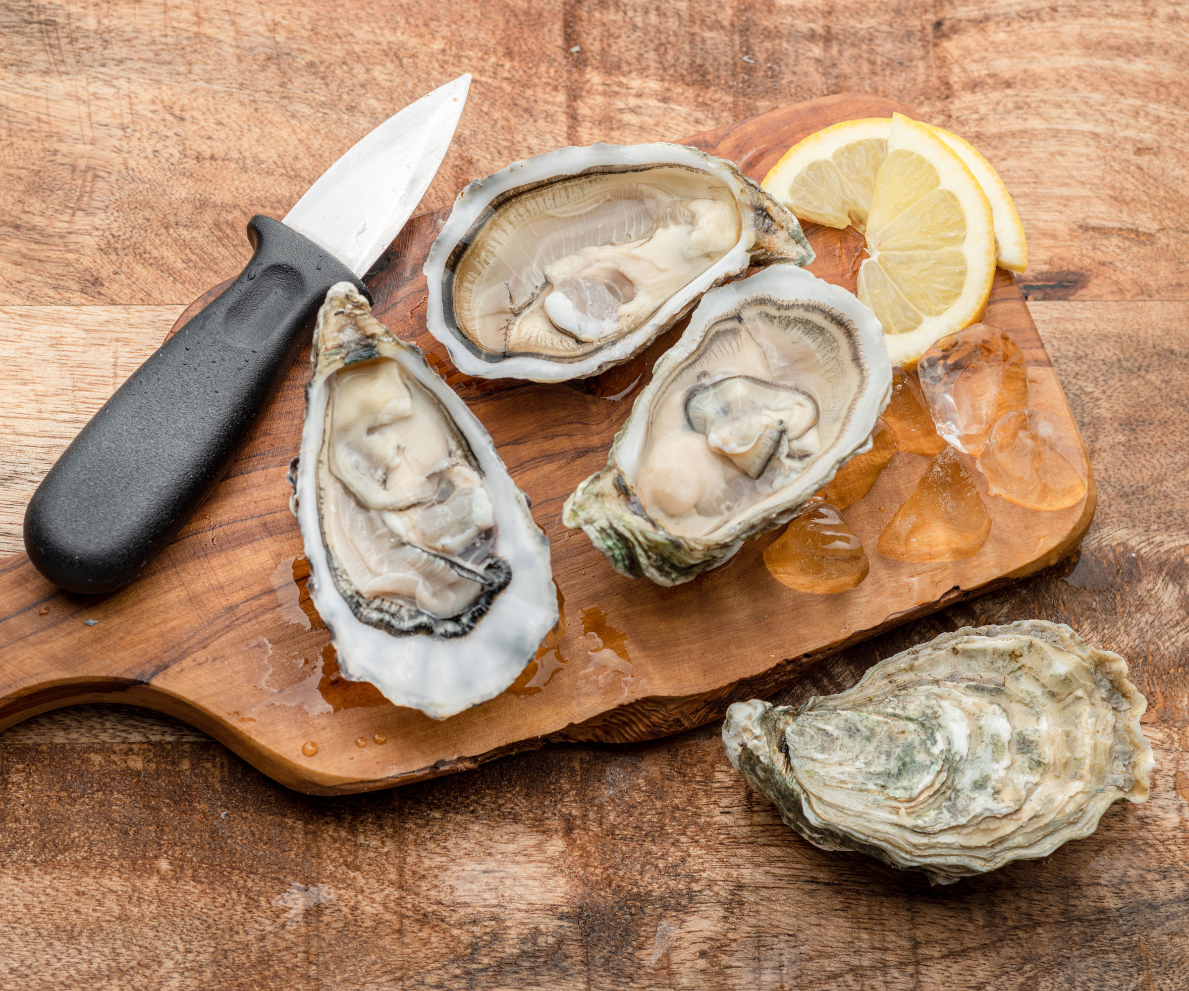oysters and knife with lemon on wooden chopping board and wooden table