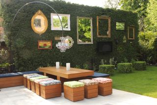 Garden space with a dining area and a series of outdoor mirrors placed along the length of a hedge