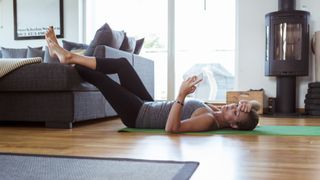 Woman lying down on the ground on a yoga mat, looking at phone and experiencing exercise burnout