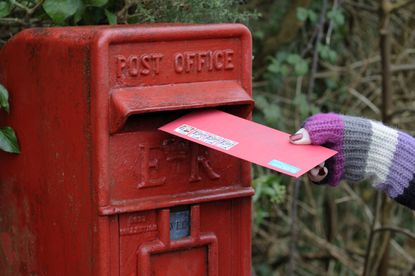 Person posting envelope into a red Royal Mail letterbox