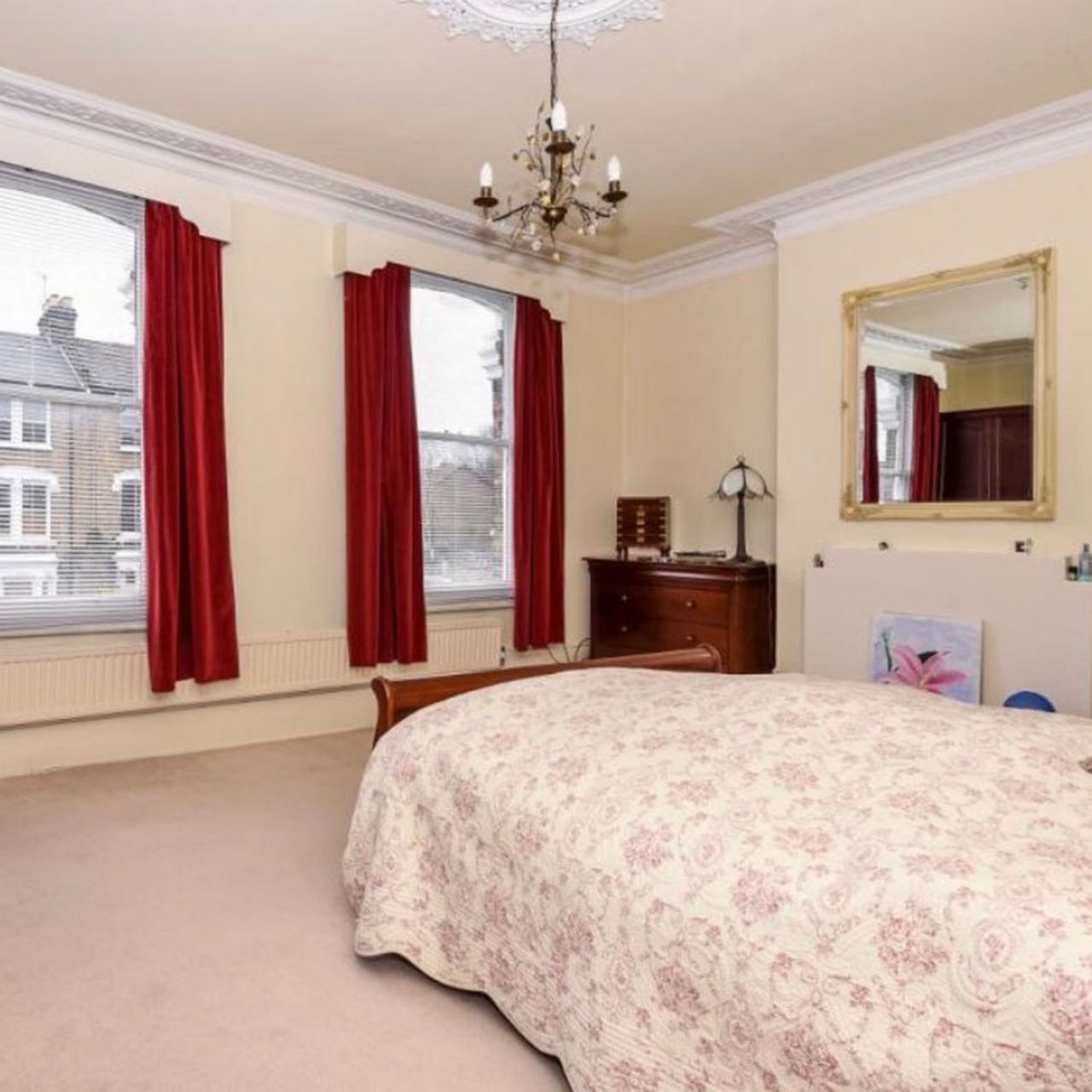 Bedroom with magnolia walls, red curtains with white pelmets and pink floral bedspread