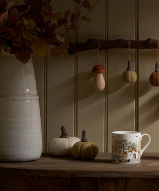 decorating with pumpkin ideas, branch with felt pumpkins and a toadstool hanging from it, mug, felt pumpkins on side, jug with autumnal flowers