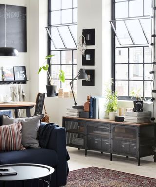 An industrial living room with a blue couch, big windows, and a black steel dresser