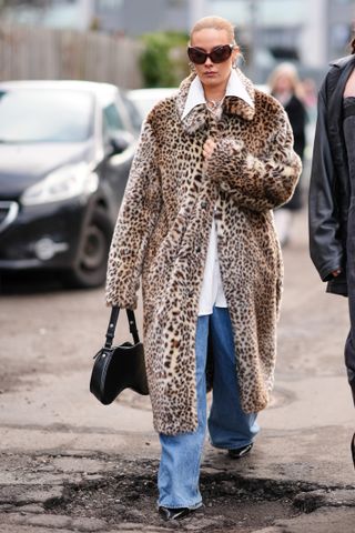 woman wearing a leopard print faux fur coat, white button down shirt, jeans, and a black bag