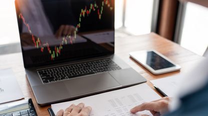 A laptop screen shows a trading graph going up and down.