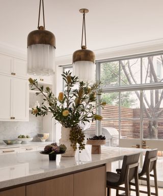 A neutral kitchen with large windows, sculptural pendants, and a marble and wood island