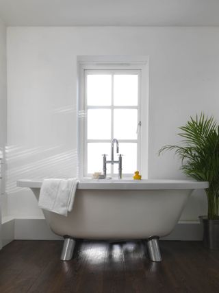 small freestanding bath in small bathroom with large window and white colour scheme