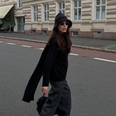 Influencer @annabelrosendahl walks down the street wearing a knitted bucket hat with a black jumper and grey trousers.