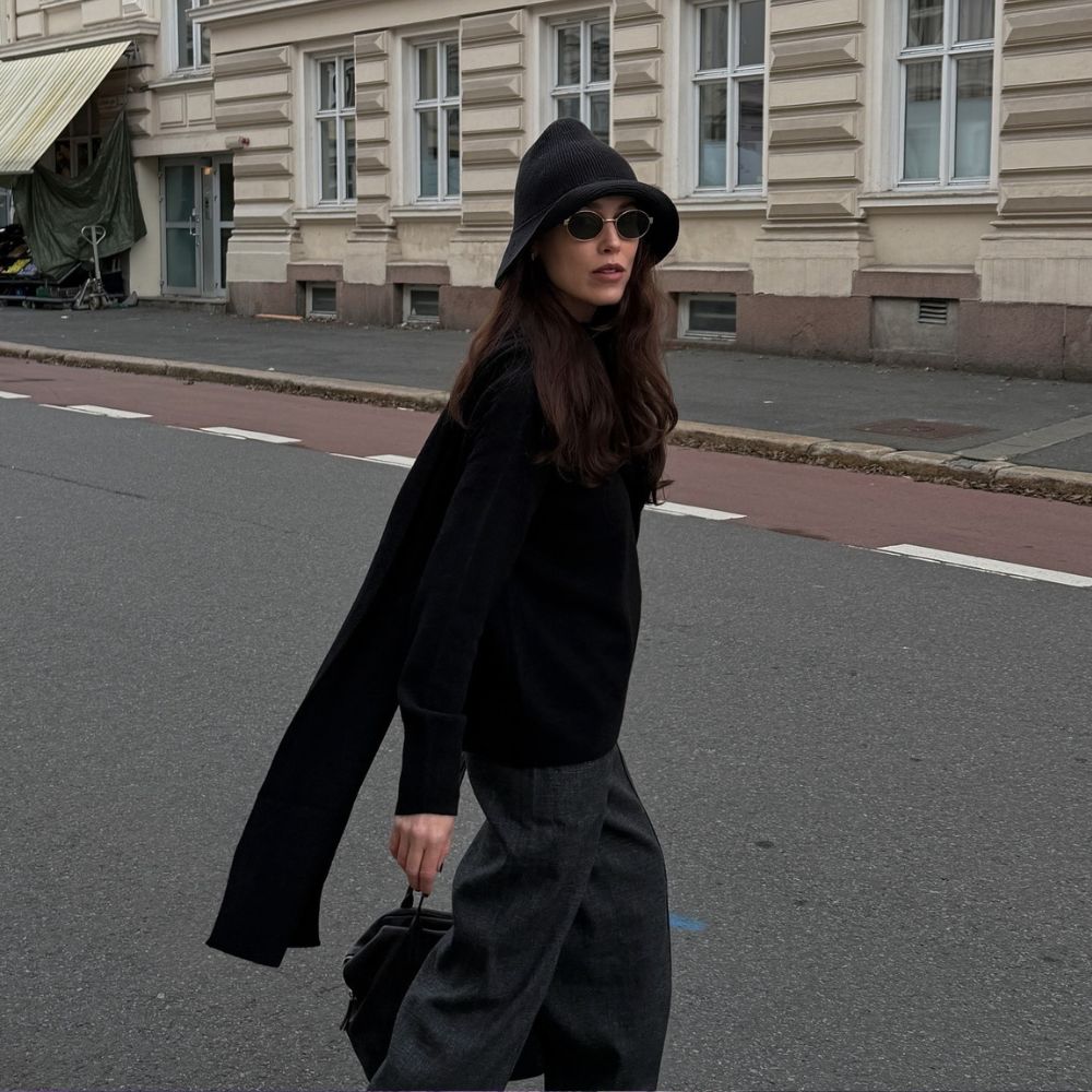 Influencer @annabelrosendahl walks down the street wearing a knitted bucket hat with a black jumper and grey trousers.