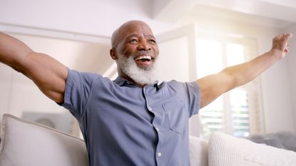 An older man celebrates while sitting on his sofa.