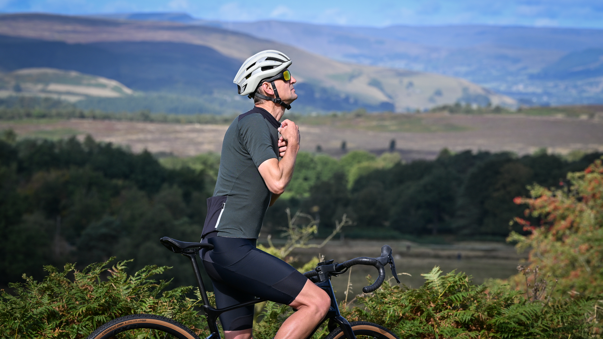 man wearing a dark green jersey and beige helmet on a black gravel bike doing up the zip on his jersey