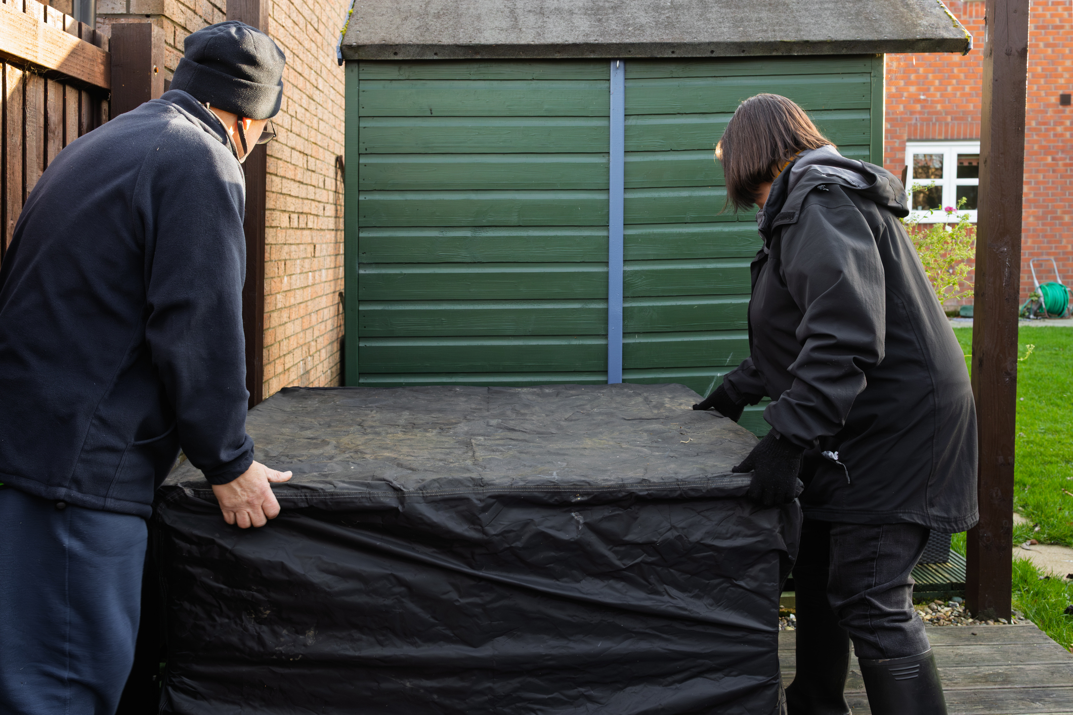 A mature couple move a covered firepit away from their home.