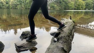 A hiker's legs as they step from log to stone crossing a river