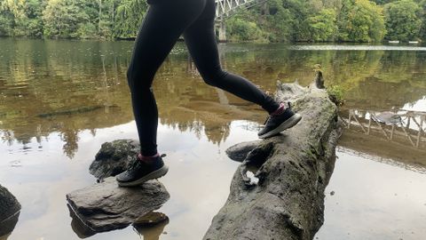 A hiker&#039;s legs as they step from log to stone crossing a river