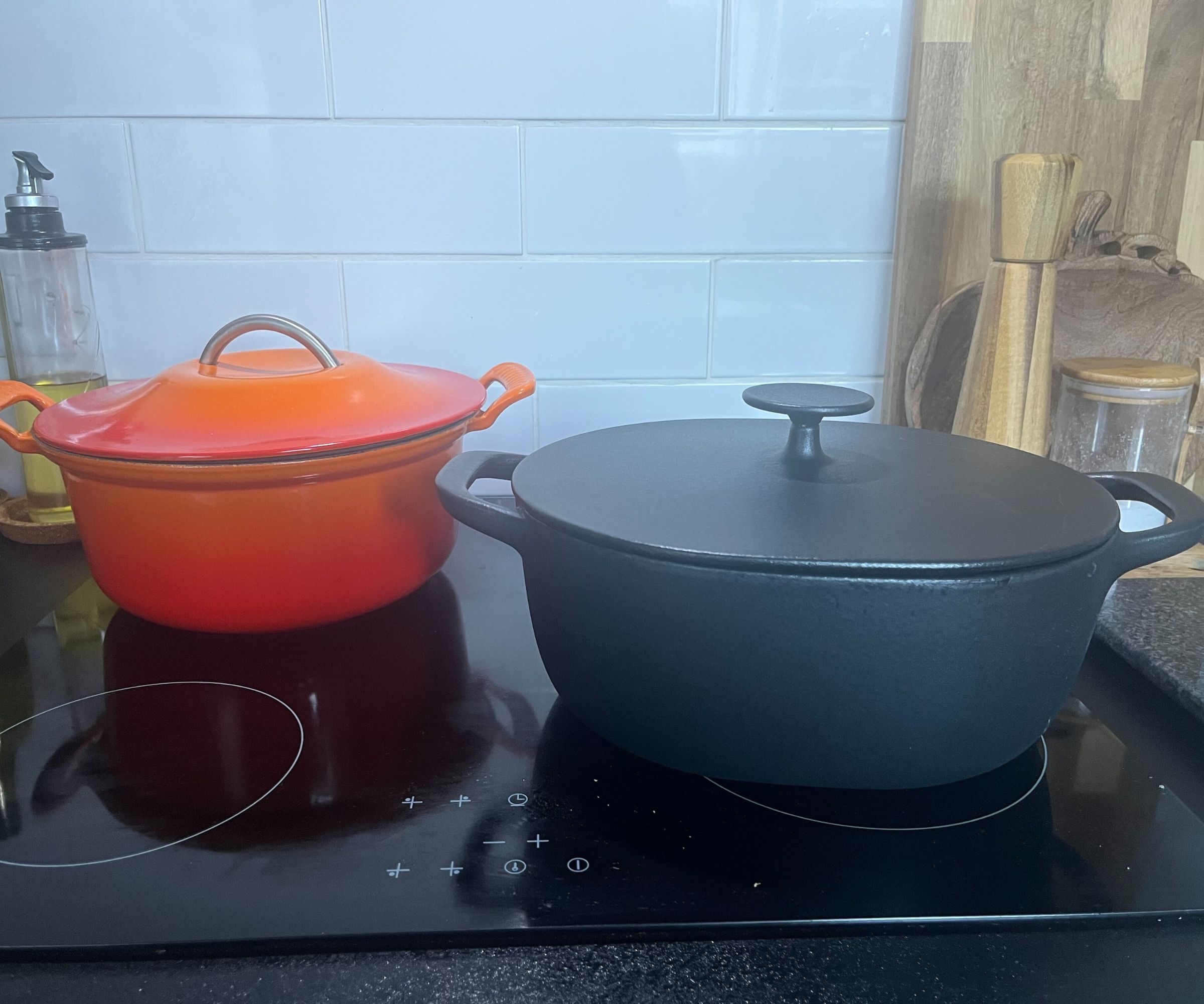 IKEA Dutch oven beside Le Creuset Dutch oven on a black electric stove, in front of a white subwaytile backsplash