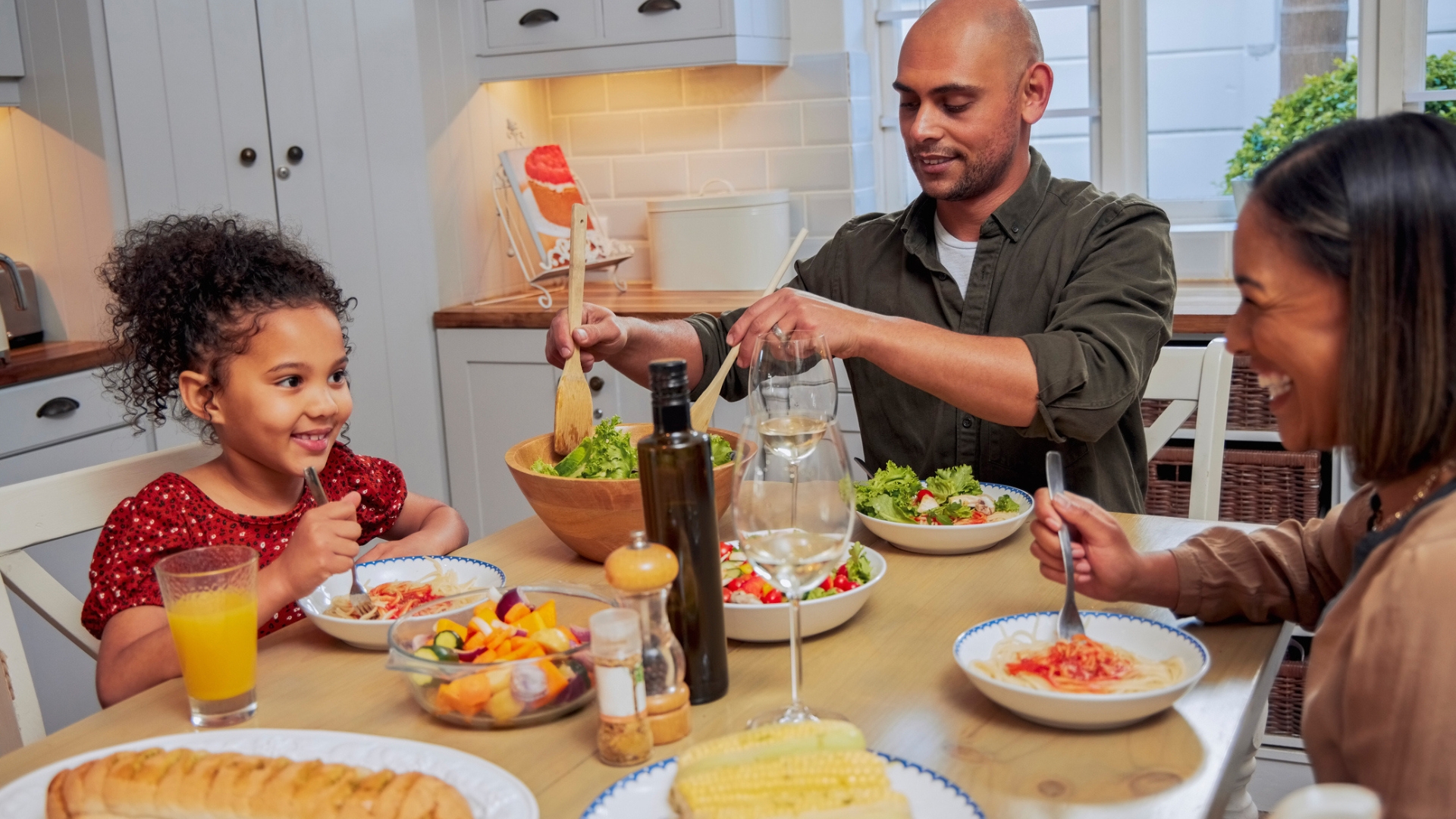 woman, man and child sitting at a table eating a meal and smiling to each other