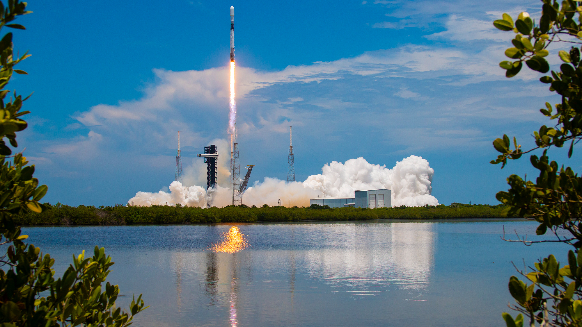 a rocket launches into a blue sky with a lake in the foreground
