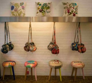 textile bags hanging above patterned stools bearing the names of the seven deadly sins