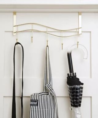 A gold over-the-door organizer with an umbrella and bags on it against a white door