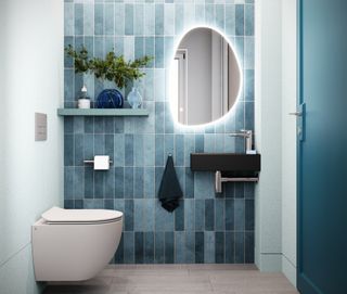 A modern bathroom with blue tiles, a white toilet and a mirror with lighting