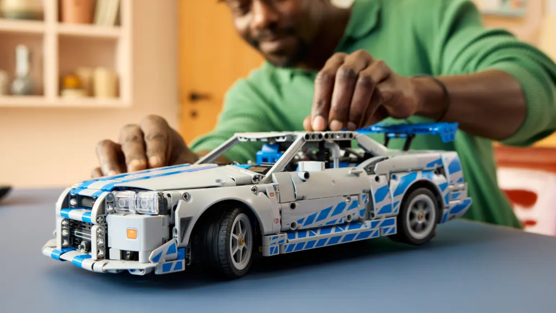 A man places a piece onto the Lego 2 Fast 2 Furious Nissan Skyline GT-R model on a table