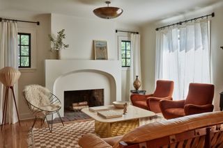 Neutral living room with stucco fireplace, checked white and terracotta rug, terracotta velvet armchairs and tan leather sofa