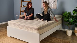 Two Tom's Guide mattress testers sat crossed legged on the Birch Luxe Natural mattress laughing and smiling