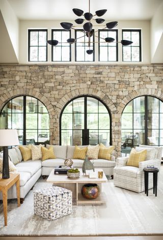 How to design a living room decor scheme with pale gray and yellow soft furnishings, large windows and a modern black chandelier.