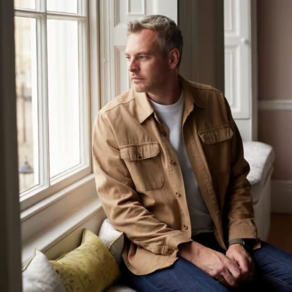 Headshot of a man looking out of a window in a light brown jacket