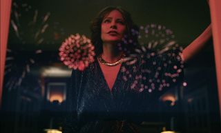 a woman (sofia vergara as griselda blanco) looks out of a window, which shows the reflection of fireworks